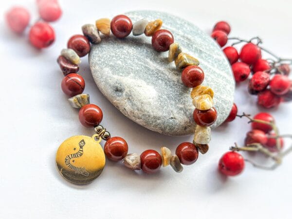 Bransoletka z czerwonego i brązowego jaspisu z przywieszką rysunkiem Beaty Pawlikowskiej Wąż Quetzalcoatl